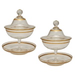 SAINT LOUIS, France - Par de compoteiras com seus presentoirs em cristal francês, translucido. Caracterizam-se pelo design clássico com frisos e acabamentos decorativos dourados nas bordas da tampa, do bojo e do presentoir. 30 x 15 cm (MT). 18 cm.