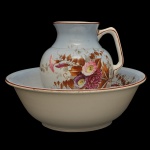 Conjunto de gomil (jarra) e bacia, em louça provavelmente europeia, sem marca. Jarra com alça encaixada dentro de uma bacia larga de lavatório. Pintura floral em tons de rosa, marrom e folhagens, com fundo em um tom azulado claro. Esses conjuntos eram usados em quartos de dormir no período vitoriano e eduardiano para a higiene pessoal diária. 26 x 15 cm (Jarra). 13 x 36 cm (bacia).