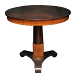 Original mesa de apresentação em madeira nobre, com tampo circular saliente dividido em 4 partes acopladas, de tonalidades contrastantes. Saia revestida e ornada por faixa com canelados verticais, acompanhando o formato. Coluna central reta e levemente afunilada, repetindo na parte inferior a faixa da saia apoiada em anelado. Base triangular com pés revirados em volutas. Apresenta sinais de uso, riscados. 78 x 85 cm.