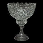 Fruteira de pé em cristal translucido e lapidado com padrões geométricos. Borda trabalhada em formato floral ondulado, bojo com lapidação em relevo estilo diamante e base facetada com pé de sustentação. Pequeno bicado. 27 x 20 cm,