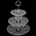 Centro de mesa com três estágios em espesso vidro translúcido com detalhes lapidados geométricos e haste central em  metal prateado. 33 x 26 cm.