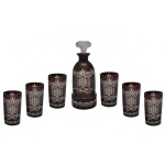 Conjunto de licoreira e copos em cristal da Boêmia, famoso pelo estilo tradicional conhecido como Ruby Cut-to-Clear (cristal duplo lapidado em tom vermelho-rubi ou vinho). Apresenta padrões geométricos e florais lapidados à mão, que removem a camada colorida externa para revelar o cristal translúcido por baixo. O conjunto é composto por uma garrafa licoreira central com tampa (25 x 10 cm) e seis copos altos 13 x 7 cm). Espólio de Josephina Penteado da Fonseca, SP.
