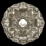 Medalhão ou salva de aparato em metal espessurado a prata,  com rica decoração em relevo de concheados e motivos florais. Formato circular e recortado, trabalhado com elementos rococó, concheados e flores repuxadas em relevo. 45 cm. Espólio de Josephina Penteado da Fonseca, SP.