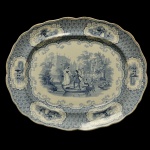 Inglaterra. Séc. XIX - Travessa de formato oval em louça inglesa decorada com a clássica técnica de monocromia em azul e branco (blue transferware). Uma ilustração detalhada de estilo bucólico ou romântico europeu, retratando figuras humanas em uma paisagem natural ou de jardim. Bordas onduladas com ricas decorações florais, padrões geométricos rendados ou pequenas vinhetas integradas na aba da travessa. 43 x 35 cm. Um pequeno carimbo azul de fábrica perto da borda superior. Marcas de uso e do tempo. Espólio de Josephina Penteado da Fonseca, SP.