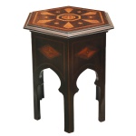 Mesa lateral, oriental em madeira nobre com tampo hexagonal saliente, ornamentado em marqueterie geométrica centralizando medalhão com adornos estilizados. Saia comprida recortada em arcos, realçada por losangos e rematada por pernas retas e lisas. 53 x 40 cm. Espólio de Josephina Penteado da Fonseca, SP.