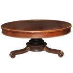 Mesa de centro em madeira nobre, com tampo circular saliente, apoiado em saia lisa com friso canelado. Coluna central tornada, montada em largos anelados superpostos. Pernas inclinadas e curvilíneas, rematadas por pés em volutas. Transição séc. XIX - séc. XX. 44 x 100 cm. Espólio de Josephina Penteado da Fonseca, SP.