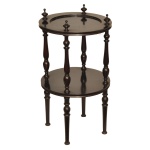 Mesa lateral redonda em estilo retrô clássico, confeccionada em madeira escura. Tampo superior circular com bordas ligeiramente elevadas e uma prateleira inferior idêntica para armazenamento extra. As superfícies são conectadas por elegantes colunas e pernas trabalhadas com detalhes torneados clássicos. O topo da mesa apresenta ponteiras ornamentais salientes acima de cada coluna de sustentação. 56 x 30 cm. Espólio de Josephina Penteado da Fonseca, SP.