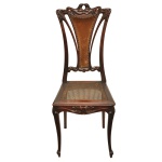 Bela e rara cadeira Art Nouveau em madeira nobre. Apresenta exuberante encosto alto, com laterais recurvas, reunidas ao topo por composição finamente esculpida com elementos fitomórficos entrelaçados. Tabela acompanhando o estilo, com segmento em couro tacheado, recortado em corneta e ladeado por hastes arqueadas. Assento em palhinha da Índia, apoiado em saia ondulada e realçada por motivos vegetais. Pernas dianteiras suavemente curvilíneas, rematadas por pés revirados sobre sapatas. 102 x 41 x 41 cm. Espólio de Josephina Penteado da Fonseca, SP.