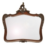 Espelho de parede, de formato retangular com laterais arqueadas, bordado por moldura em madeira lustrada e realçada por adornos fitomórficos e volutas. Frontão encimado por composição com arabesco vazado ao topo. 42 x 58 cm (MI). 70 x 73 cm (ME). Espólio de Josephina Penteado da Fonseca, SP.