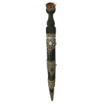 Autêntico Dirk Escocês (Scottish Dirk) antigo, uma adaga tradicional de vestimenta das Terras Altas da Escócia completa com seus acessórios de bainha. Possui uma lâmina longa de gume único com o dorso trabalhado em padrão serrilhado. A empunhadura é esculpida em madeira escura imitando o tradicional padrão de trançado de cesto. O pomo no topo é coroado com uma grande pedra de quartzo citrino lapidado. Revestida de couro preto com guarnições metálicas decorativas em metal prateado, ricamente cinzeladas com motivos de cardos que são o símbolo nacional da Escócia. O conjunto inclui as duas pequenas ferramentas que se encaixam em compartimentos dedicados na própria bainha: uma faca pequena (utility knife) e um garfo de dois dentes acompanhante. Suas empunhaduras repetem o mesmo design trançado do punhal princip. 49 cm.