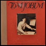 Raro box set institucional de Tom Jobim, lançado em 1987. O conjunto de colecionador foi idealizado pela CBPO (Companhia Brasileira de Projetos e Obras). O box completo é composto por: Álbum Duplo (2 LPs): Traz uma seleção sofisticada com 24 faixas que cobrem momentos fundamentais da carreira do maestro. Livro Biográfico: Um livro de luxo escrito pelo renomado jornalista Sérgio Cabral, Por ter sido desenvolvido como um brinde corporativo de fim de ano para clientes e parceiros, ele não foi comercializado em lojas na época, tornando-se um item altamente valioso entre colecionadores de MPB e Bossa Nova. Caixa rígida de formato quadrado com abertura estilo estojo para acomodar os discos e a publicação.
