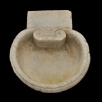 Antiga pia batismal em mármore branco, com bacia circular, ornamentada na parte interna por adorno com volutas centralizando flor de lis. Apresenta, no mesmo lado, suporte retangular externo para fixação em parede.12 x 52 x 45 cm.