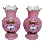 Par de pequenos vasos em vidro opalinado rosa. Bojos globulares ornados em policromia por arranjos florais. Gargalos cônicos encimados por bordas dentadas e douradas. Bases circulares lisas. 11 x 7 x 5 cm.