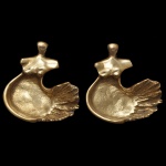 ODETTE EID (Libano, 1922  São Paulo, 2019) - Par de vide poche em metal dourado e polido retratando uma figura feminina estilizada. Apresenta torso de mulher nu que se funde fluidamente a uma cavidade em formato de concha com relevos detalhados. Ass verso. 3 x 13 x 14 cm.