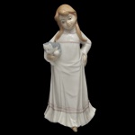 DArt SA. - Estatueta de porcelana brilhante de manufatura espanhola retratando uma jovem menina segurando um gatinho. No verso marca da manufatura. Representação clássica em tons suaves de branco e bege, com detalhes delicados nas vestes da figura e no animal em seus braços.