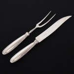 FAQUEIRO, conjunto trinchante com duas (2) peças para carnes, confeccionadas em aço inox com cabo em metal prateado, ornamentação relevada no padrão Império Napoleônico em frisos intercalados por X com terminações em concha e laçarote, manufatura FRACALANZA (tradição desde 1884), sendo: 1 garfo e 1 faca, medindo a maior peça 27,5 cm comprimento, vide foto.