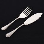 FAQUEIRO, dois (2) talheres de servir peixe, confeccionados em metal prateado, ornamentação relevada no padrão Império Napoleônico em frisos intercalados por X com terminações em concha e laçarote, manufatura FRACALANZA (tradição desde 1884),  sendo: 1 espátula, medindo 28,5 cm comprimento e 1 garfo, medindo 24 cm comprimento, vide foto.