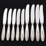 FAQUEIRO, nove (9) facas, confeccionadas em metal prateado, ornamentação relevada no padrão Império Napoleônico em frisos intercalados por X com terminações em concha e laçarote, lâminas em aço inox, manufatura WOLFF (tradição desde 1894), sendo: 5 de sobremesa, medindo 20,5 cm comprimento; 4 de serviço, medindo 24 cm comprimento, vide foto.