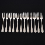 FAQUEIRO, doze (12) garfos de sobremesa, confeccionados em metal prateado, ornamentação relevada no padrão Império Napoleônico em frisos intercalados por X com terminações em concha e laçarote, sendo: 6 da manufatura FRACALANZA (tradição desde 1884), medindo 14,5 cm comprimento; 6 da manufatura WOLFF (tradição desde 1894), medindo 14,5 cm comprimento, vide foto.