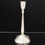 METAL PRATEADO, um (1) castiçal com base canelada terminando em degraus, fuste em coluneta afinando para cima, amarração em esferas, bobeche no formato de tulipa com ligeira mossa, sem marca de manufatura aparente, medindo 24 cm altura, vide foto.