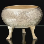 METAL PRATEADO, um (1) vaso bojudo, ornamentação relevada no padrão Império Otomano, com primoroso cinzelado vegetalista e geometrizado, base trípode terminando em sapatas. Marca na base H. V. - Made in Índia, medindo 12 cm diâmetro e 9 cm altura, vide foto.