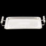 METAL PRATEADO, uma (1) bandeja retangular, fundo ornado em baixo relevo com pérgulas, volutas e elementos vegetalistas, alças relevadas em fumo de rolo, sem marca de manufatura aparente, medindo 33 x 25,5 cm mais as alças, vide foto.
