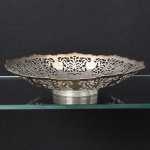 METAL PRATEADO, uma (1) fruteira de pé baixo, borda recortada e vazada em silhuetas vegetalistas, base canelada na horizontal, marca WOLFF (tradição desde 1894), medindo 26,5 cm diâmetro e 5,5 cm altura, vide foto.