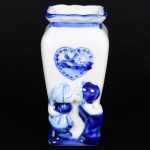 PORCELANA HOLANDESA, um (1) vaso quadrangular, modelagem representando casal de crianças se beijando, ornamentação pintada a mão na técnica blue and white, representando paisagem com marina e moinhos dentro de um coração e elementos vegetalistas, característica da região de Delft, medindo 9,5 cm altura, vide foto.