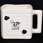 FAIANÇA, uma (1) cremeira retangular para pacote de leite (vaca da caixinha), ornamentação pintada a mão representando vaca holandesa e a legenda leite, sem marca de manufatura aparente, medindo 12,5 x 8,5 x 12 cm mais a alça, vide foto.