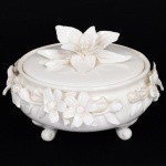PORCELANA, um (1) pote com tampa, tonalidade branca, ornamentação do bojo e pega da tampa, relevados em flores com pequenas perdas no bojo, base trípode com terminações em volutas, medindo aproximadamente 12,5 cm diâmetro e 9 cm altura, vide foto.