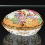 PORCELANA, uma (1) caixa oval, ornamentação policromada com flores, faixas na tonalidade azul cobalto, arremates a ouro, marca Fine Porcelain Hand Painted  24K Gold Deco Collections LIMOGES, monture em metal dourado, medindo 9 x 6,5 x 4,5 cm, vide foto.