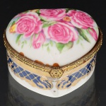 PORCELANA, uma (1) caixa no formato de coração, ornamentação policromada com rosas, faixas na tonalidade azul cobalto, arremates a ouro, marca Fine Porcelain Hand Painted  24K Gold Deco Collections LIMOGES, monture em metal dourado, medindo 6,5 x 6 x 4 cm, vide foto.