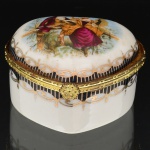 PORCELANA, uma (1) caixa no formato de coração, ornamentação policromada com cena de galanteio, faixas na tonalidade azul cobalto, arremates a ouro, marca Fine Porcelain Hand Painted  24K Gold Deco Collections LIMOGES, monture em metal dourado, medindo 6,5 x 6 x 4 cm, vide foto.