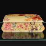 PORCELANA, uma (1) caixa retangular com tampa, ornamentação policromada representando flores, sobre fundo na tonalidade amarela, assinada M. Yvonne, medindo 19 x 14 x 6 cm, sem marca de manufatura aparente, vide foto.