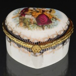 PORCELANA, uma (1) caixa no formato de coração, ornamentação policromada com cena de galanteio, faixas na tonalidade azul cobalto, arremates a ouro, marca Fine Porcelain Hand Painted  24K Gold Deco Collections LIMOGES, monture em metal dourado, medindo 6,5 x 6 x 4 cm, vide foto.