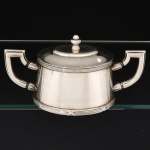 METAL PRATEADO, um (1) açucareiro com ornamentação no padrão Império Napoleônico com frisos intercalados por X, pega da tampa na forma de carrapeta, marca FRACALANZA (tradição desde 1884), medindo 19,5 cm comprimento de uma alça a outra, vide foto.