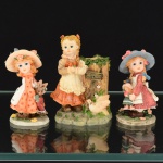 ESCULTURAS, três (3) figurativas distintas confeccionadas em resina e policromadas, representando meninas com boneca, urso de pelúcia e pombas, uma delas é um paliteiro, medindo a maior 9,5 cm altura, vide foto.
