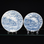 FAIANÇA INGLESA, dois (2) pratos distintos, tonalidade azul e branca, marca ROYAL WESSEX (WESSEX CERAMIC TILING LTD., Oak Apple House North Street, Milborne Port, Sherborne, England), sendo: 1 fundo e 1 raso, borda modelada em caneluras espiraladas, ornado com paisagem de vilarejo com casarios, carruagem puxada por duas parelhas de cavalos e figuras, medindo respectivamente 22 cm e 25,5 cm diâmetro, vide foto.