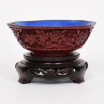 ARTE ORIENTAL, um (1) bowl tipo tigela com laca relevada em flores, tonalidade vermelha, parte interna com esmalte na tonalidade azul, acompanha peanha em madeira torneada, entalhada em vazados e ebanizada, medindo 12,5 cm diâmetro e 4,5 cm altura, altura total com a peanha inclusa 8,5 cm, vide foto.