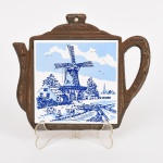 DIVERSOS, um (1) descanso de panela com estrutura em ferro fundido representando bule, aplique em azulejo representando paisagem com moinho, tonalidade azul e branca, possui quebrado e colado, medindo 15 x 17 cm, vide foto.