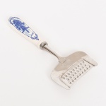 DIVERSOS, um (1) ralador de queijo, marca HENRI WILLIG  Holland, confeccionado em aço inox, cabo em porcelana pintada a mão na técnica blue and white, representando paisagem de marina com barcos, moinho e pássaros, medindo 19 cm comprimento, vide foto.