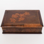 DIVERSOS, uma (1) antiga caixa em madeira, ornada com marchetaria floral, perdas de placagem, falta a chave, selo da NEUGART, medindo 31 x 21 x 8,5 cm, demanda restauro, vide foto.