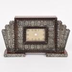 RELÓGIO, um (1) antigo de mesa, cornija ou estante, marca ANGELUS (fundada em 1891 em Le Locle, pelos irmãos Albert Stolz e Gustav Stolz; em 1905 ganhou sua primeira premiação foi medalha de ouro na Exposição de Liege na Bélgica; funciona até a atualidade), gabinete confeccionado em madeira e placagem de jacarandá, apliques em prata relevada em flores, padrão Art Deco, falta a máquina que seria de corda para 8 dias, medindo 16,5 x 15 x 6,5 cm, vide foto.