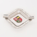 MILITARIA, um (1) cinzeiro, confeccionado em aço inox na técnica de estamparia mecanizada, borda relevada em flores e volutas, parte central esmaltada com Brasão de Armas do 20 Batalhão de Caçadores, Maceió, AL, medindo 8 x 8 cm, selo da Mil Brindes Indústria e Comércio Ltda., vide foto.