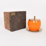 VIDRO, um (1) baleiro, incolor e translúcido, esmaltação interna na tonalidade laranja, tampa e presentoir em folha de flandres dourada, marca REGÊNCIA, acondicionado na caixa, não aparenta uso, medindo 16 cm altura, vide foto.