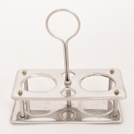 AÇO INOX, um (1) suporte galheteiro, faltam as galhetas e os polvilhadores, sem marca de manufatura aparente, medindo 21 x 11 x 21 cm, vide foto.