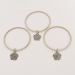 BIJUTERIA, três (3) pulseiras de argola com penduricalhos vazados em flores estilizadas, confeccionadas em metal prateado, medindo 6,5 cm diâmetro, vide foto.