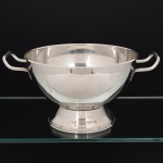 AÇO INOX, uma (1) fruteira de pé baixo com alças, lisa, formato de meia esfera, marca no verso parcialmente legível, não identificada, medindo 22,5 cm diâmetro mais as alças e 14 cm altura, vide foto.