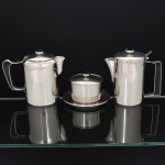 AÇO INOX, três (3) itens da marca WOLFF (tradição desde 1894), cilíndricos, detalhes em polímero, sendo: 1 bule de café; 1 bule de chá; 1 manteigueira com presentoir e tampa, recipiente em aço da marca HÉRCULES adaptado no lugar do cristal, medindo a maior peça 14,5 cm altura, vide foto.