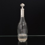 PRATA FRANCESA E CRISTAL, uma (1) antiga garrafa licoreira, lapidação dita dedão, manufatura CRISTALERIE BACCARAT (fundada em 1765 pelo Bispo de Metz na região de Baccarat como Verrerie de Saint Anne; em 1815 foi vendida, junto com outras Verreries da região, para Gabriel D'Artigues e virou Voneche-Baccarat, passando a fabricar cristal de alta qualidade; em 1822 foi vendida e virou Compagnie des Cristalleries de Baccarat, mantendo o nome Voneche até 1843, atualmente é a Cristallerie mais importante da França), monture canelado com os seguintes punções: HL (ourives Henry Lapeyre, ativo entre 1895 e 1923, estabelecido à época na Rue Meslay  Paris); Tete de Mercury (garantia do teor da prata 950 milésimos), possui mossas, peso aproximado somente da prata 100 gr., medindo 31,5 cm altura, vide foto.